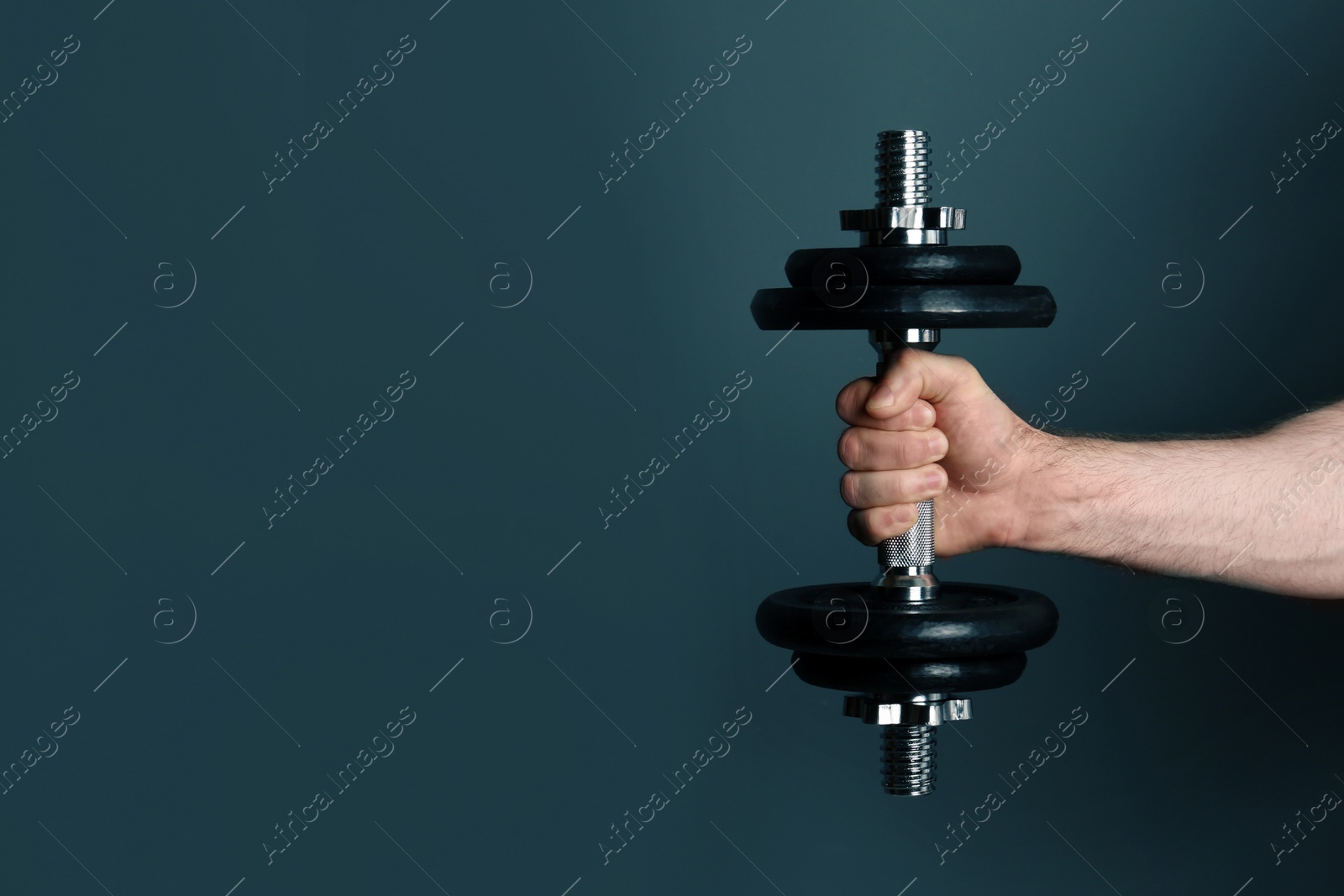 Photo of Male athlete holding metal dumbbell on color background. Space for text