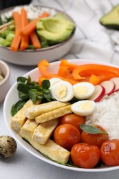 Delicious poke bowl with basil, vegetables, eggs and tofu on light grey table