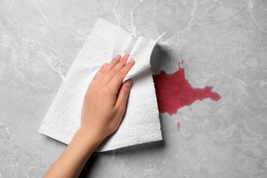 Photo of Woman wiping spilled juice with paper napkin on grey surface, top view