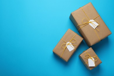 Photo of Parcels wrapped in kraft paper with tags on light blue background, flat lay. Space for text