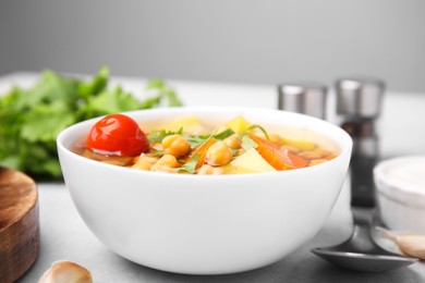 Tasty chickpea soup in bowl served on light grey table, closeup