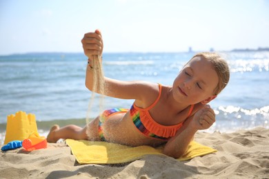 Little girl playing with sand on beach near sea
