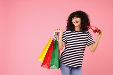 Photo of Happy young woman with shopping bags and stylish sunglasses on pink background. Space for text