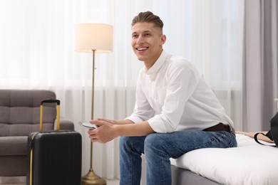 Smiling guest with smartphone relaxing on bed in stylish hotel room