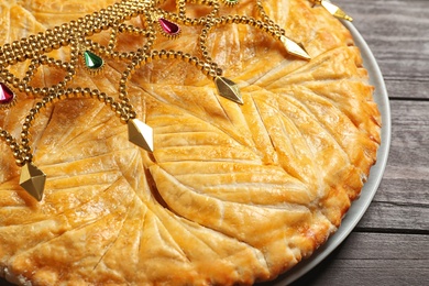 Photo of Traditional galette des rois with decorative crown on wooden table, closeup