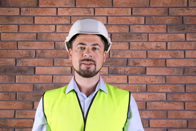 Photo of Male industrial engineer in uniform on brick wall background. Safety equipment