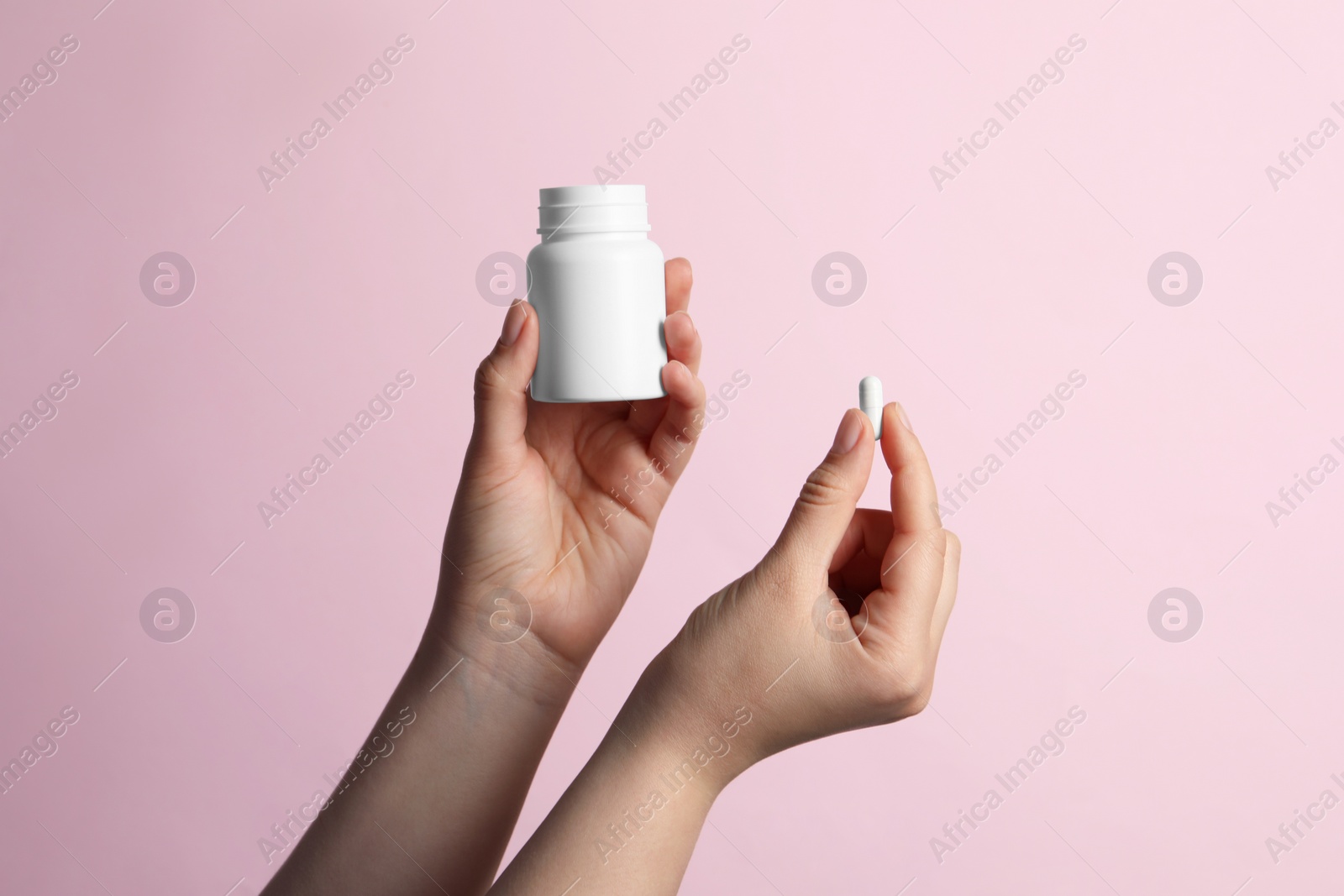 Photo of Woman holding pill and bottle on pink background, closeup