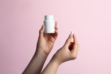 Photo of Woman holding pill and bottle on pink background, closeup