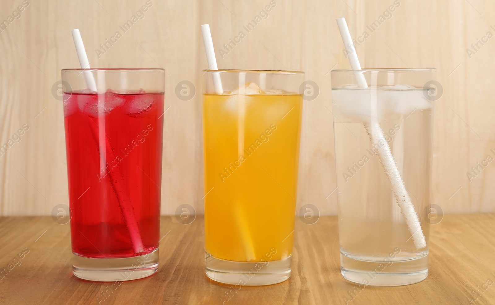 Photo of Glasses of different refreshing soda water with ice cubes and straws on wooden table