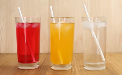 Photo of Glasses of different refreshing soda water with ice cubes and straws on wooden table