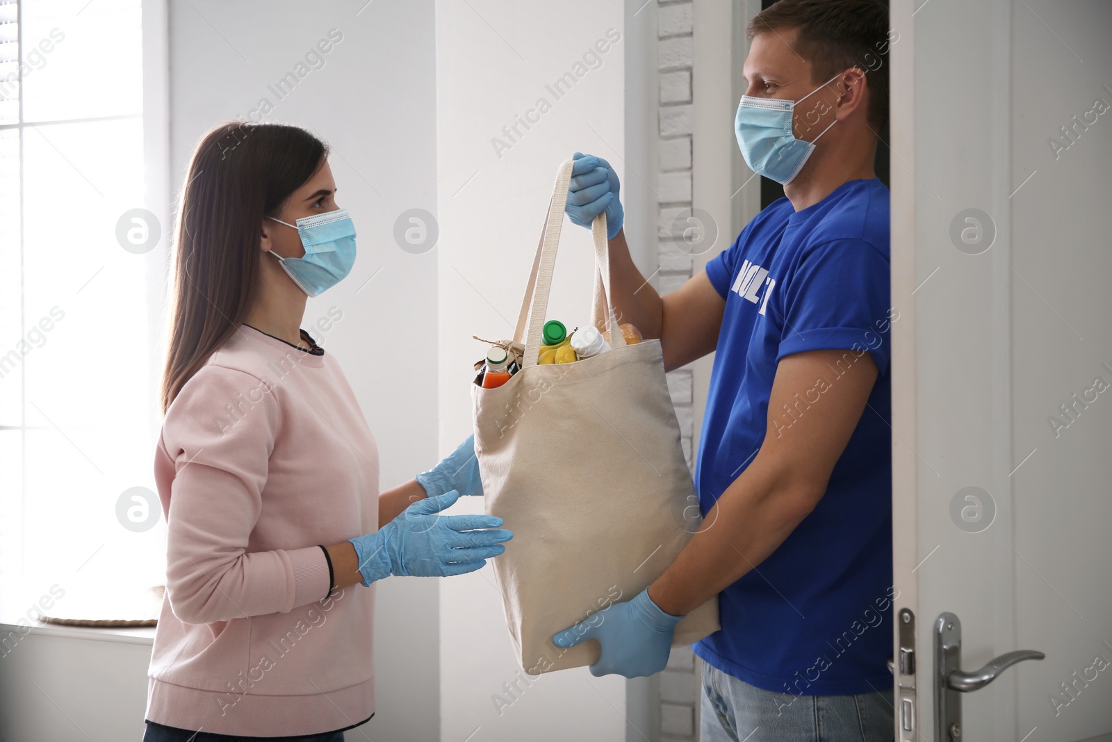 Photo of Male volunteer giving bag with products to woman indoors. Aid during coronavirus quarantine