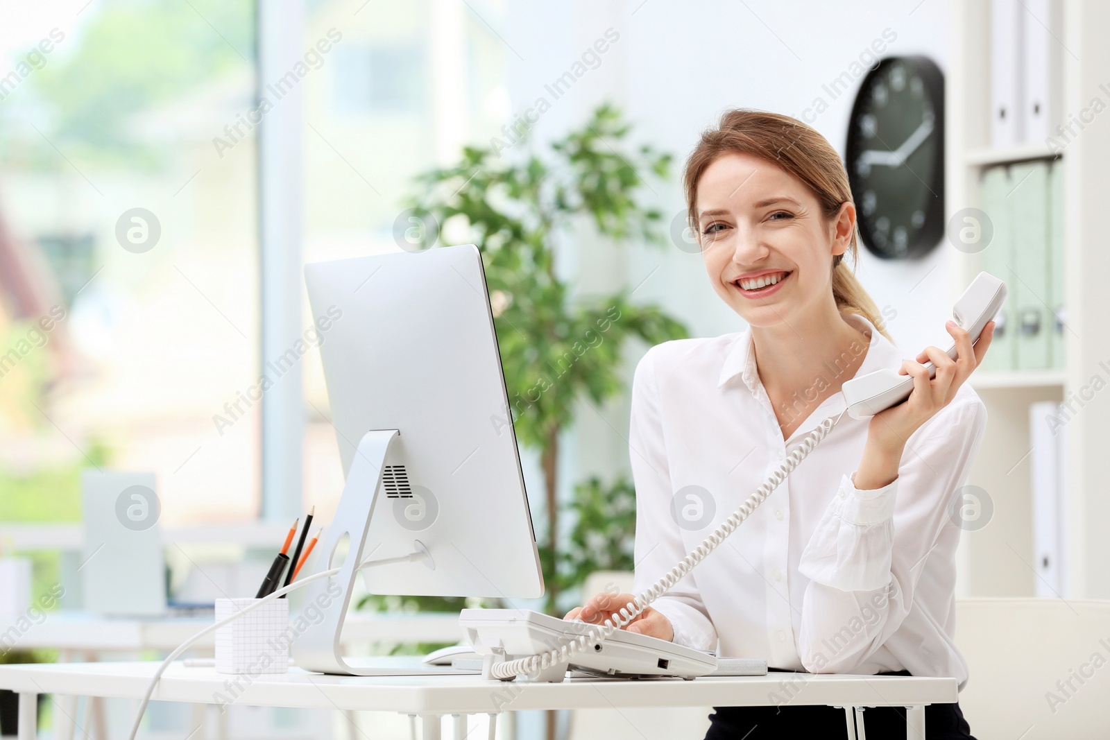 Photo of Female receptionist talking on phone at desk in office