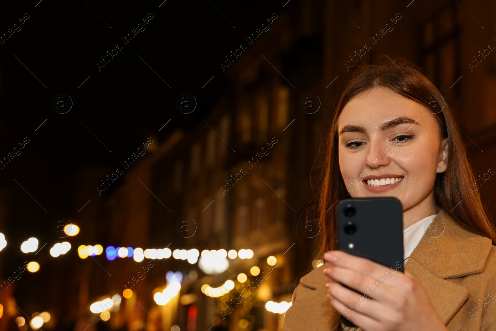 Photo of Smiling woman using smartphone on night city street. Space for text