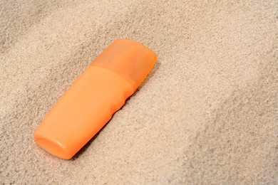 Photo of Bottle with sun protection spray on sandy beach, closeup. Space for text