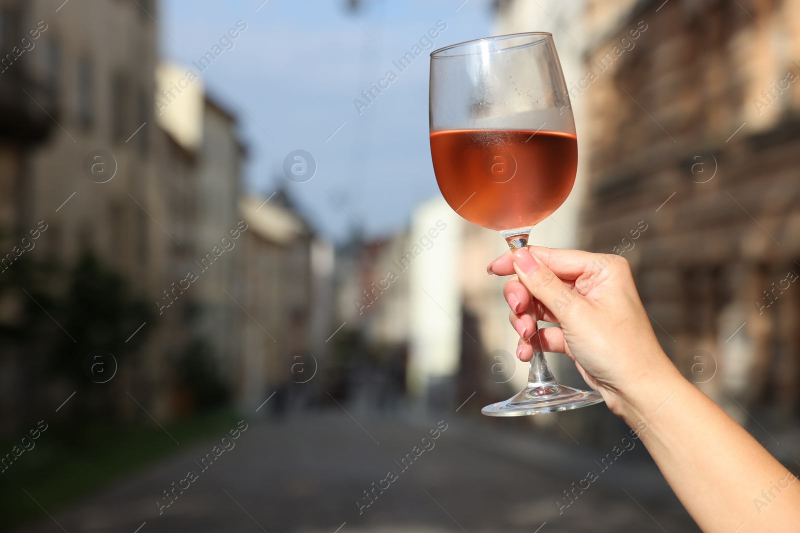 Photo of Woman holding glass of rose wine outdoors, closeup. Space for text