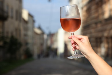 Woman holding glass of rose wine outdoors, closeup. Space for text