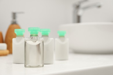 Mini bottles of cosmetic products on white countertop in bathroom. Space for text