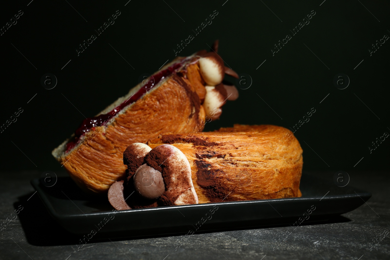 Photo of Round croissant with jam, cream and chocolate chips on grey table. Tasty puff pastry