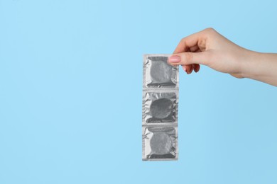 Photo of Woman holding condoms on light blue background, closeup. Space for text