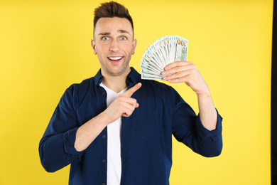 Emotional man with cash money on yellow background