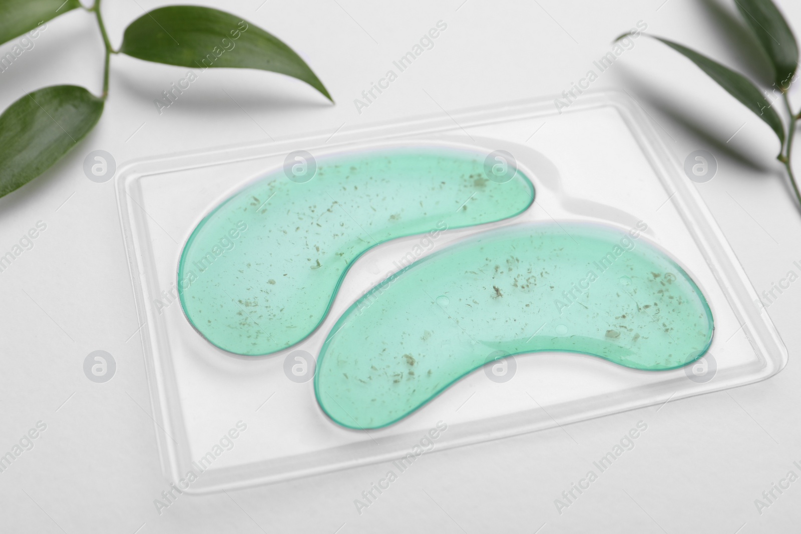 Photo of Package with under eye patches and green twigs on white background, closeup. Cosmetic product