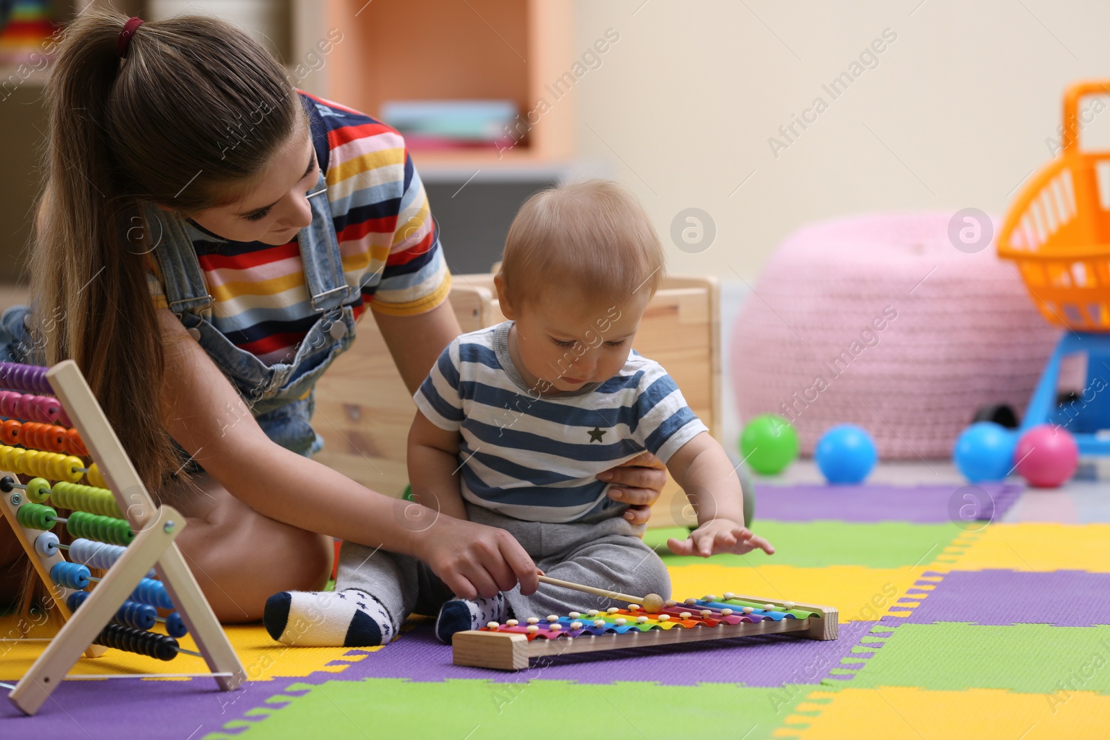 Photo of Teen nanny and cute little baby playing with xylophone at home