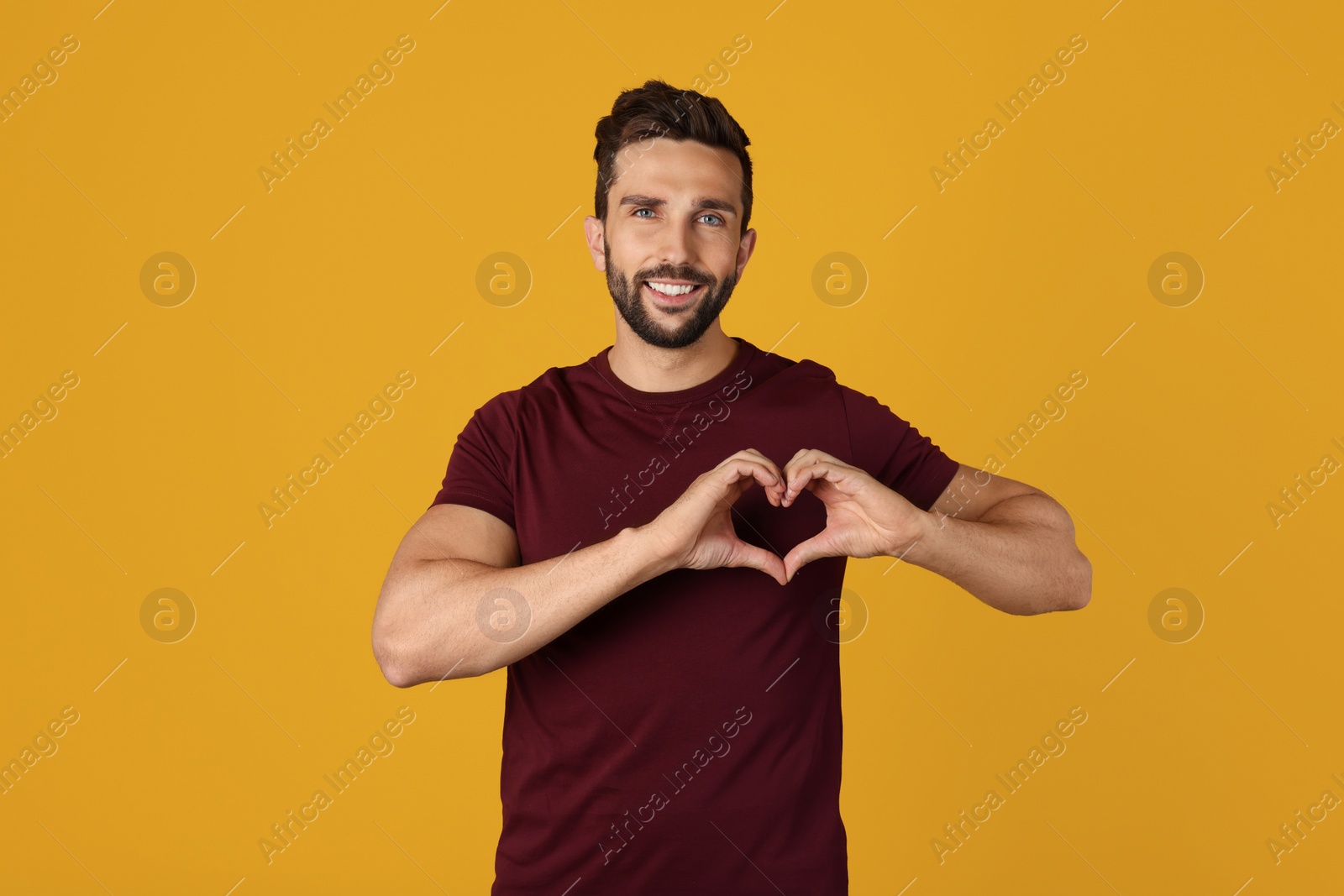 Photo of Happy man making heart with hands on yellow background