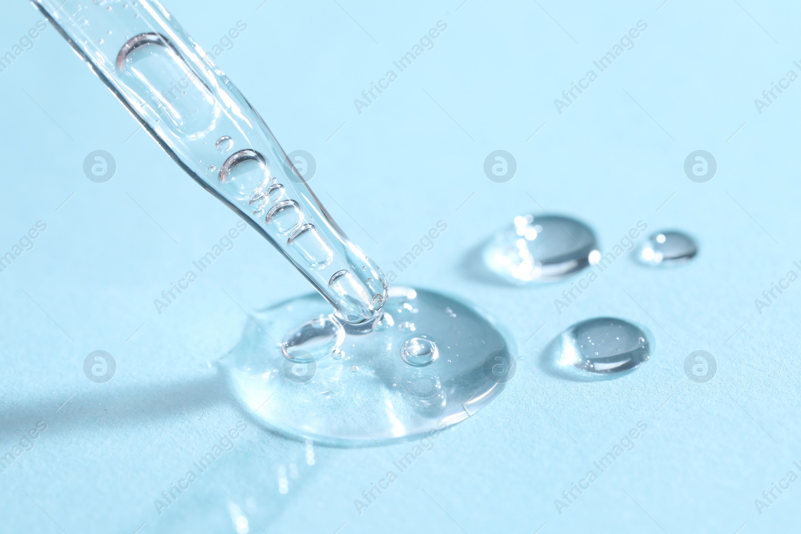 Photo of Glass pipette and transparent liquid on light blue background, closeup