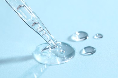 Photo of Glass pipette and transparent liquid on light blue background, closeup