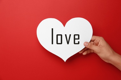 Image of Woman holding paper heart with word Love on red background, closeup