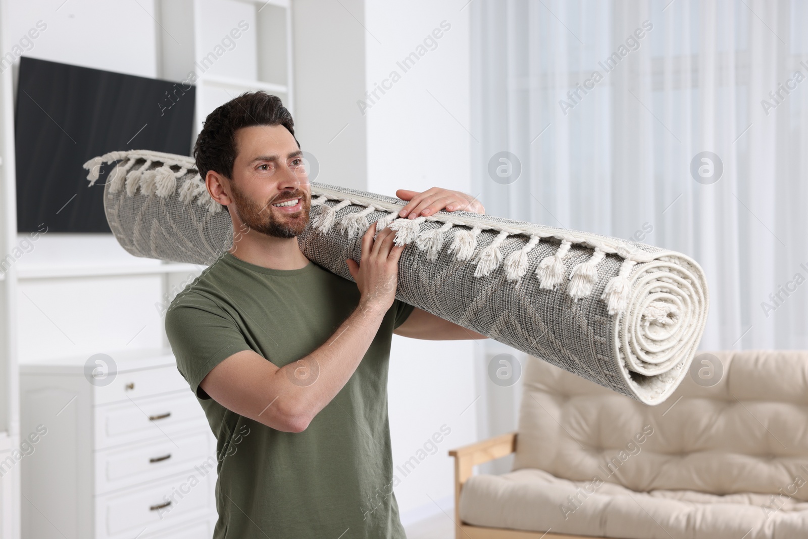 Photo of Smiling man holding rolled carpet in room