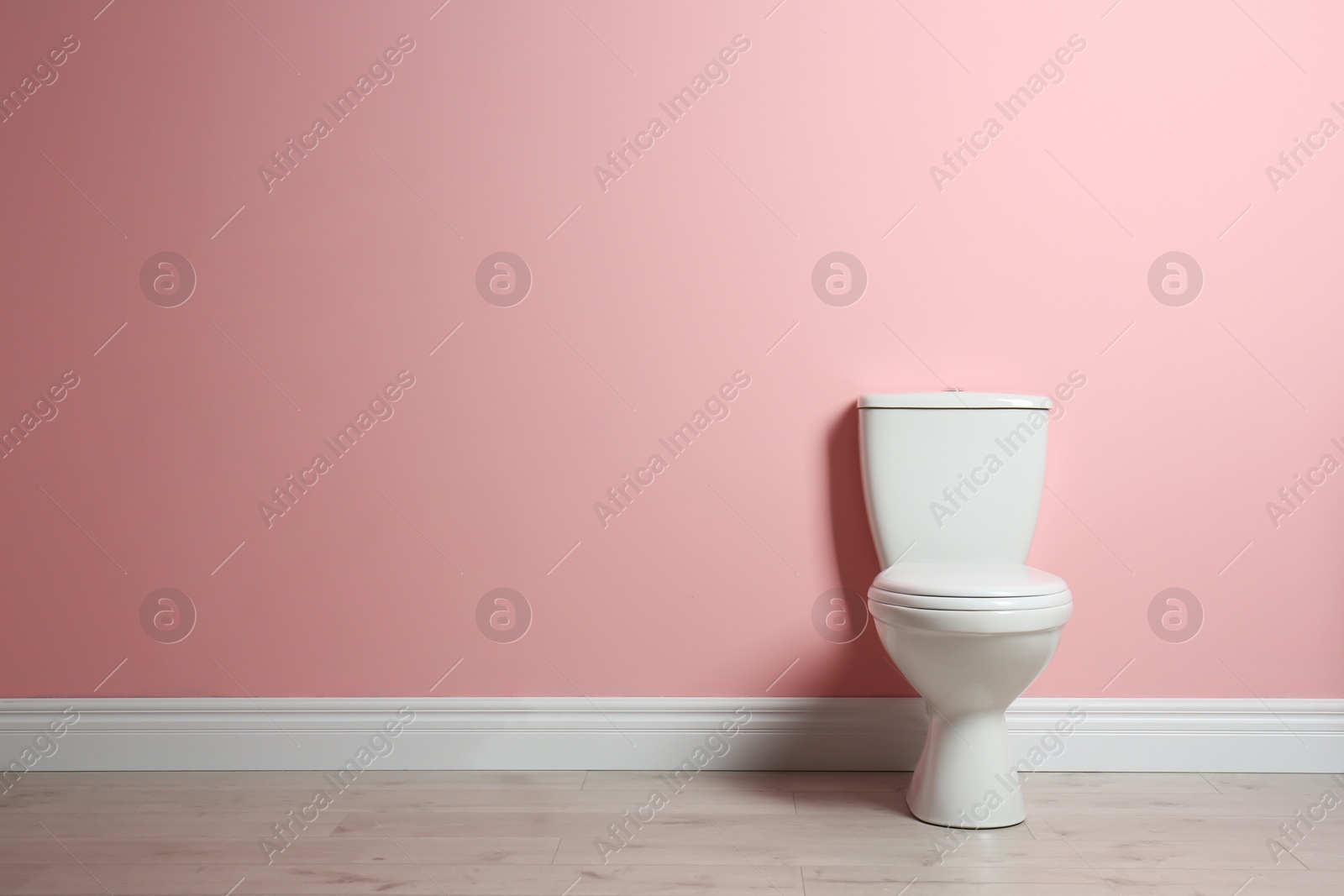Photo of New ceramic toilet bowl near color wall with space for text