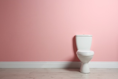 Photo of New ceramic toilet bowl near color wall with space for text