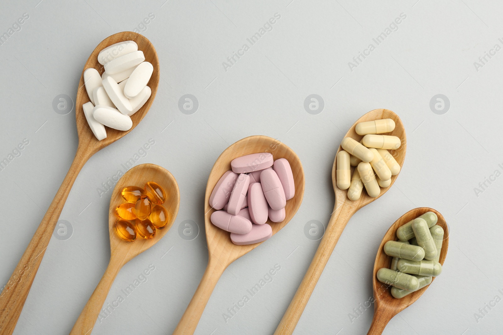 Photo of Different vitamin pills in spoons on light grey background, flat lay. Health supplement