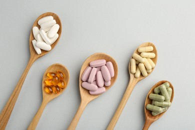 Different vitamin pills in spoons on light grey background, flat lay. Health supplement