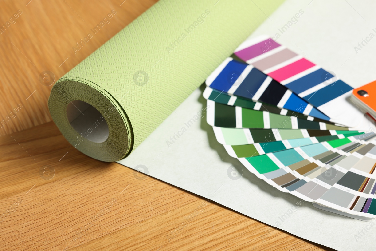 Photo of Green wallpaper roll and color palette samples on wooden table