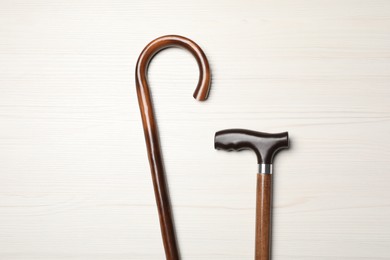 Photo of Walking canes on white wooden background, flat lay