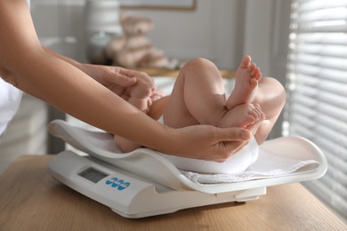 Young woman weighting her cute baby at home, closeup. Health care