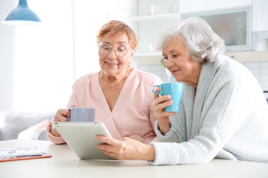 Elderly women using tablet PC at table in kitchen