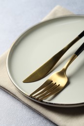 Stylish golden cutlery, plate and napkin on grey table