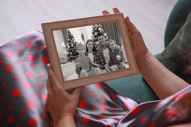 Woman holding frame with black and white photo portrait of her family indoors, closeup
