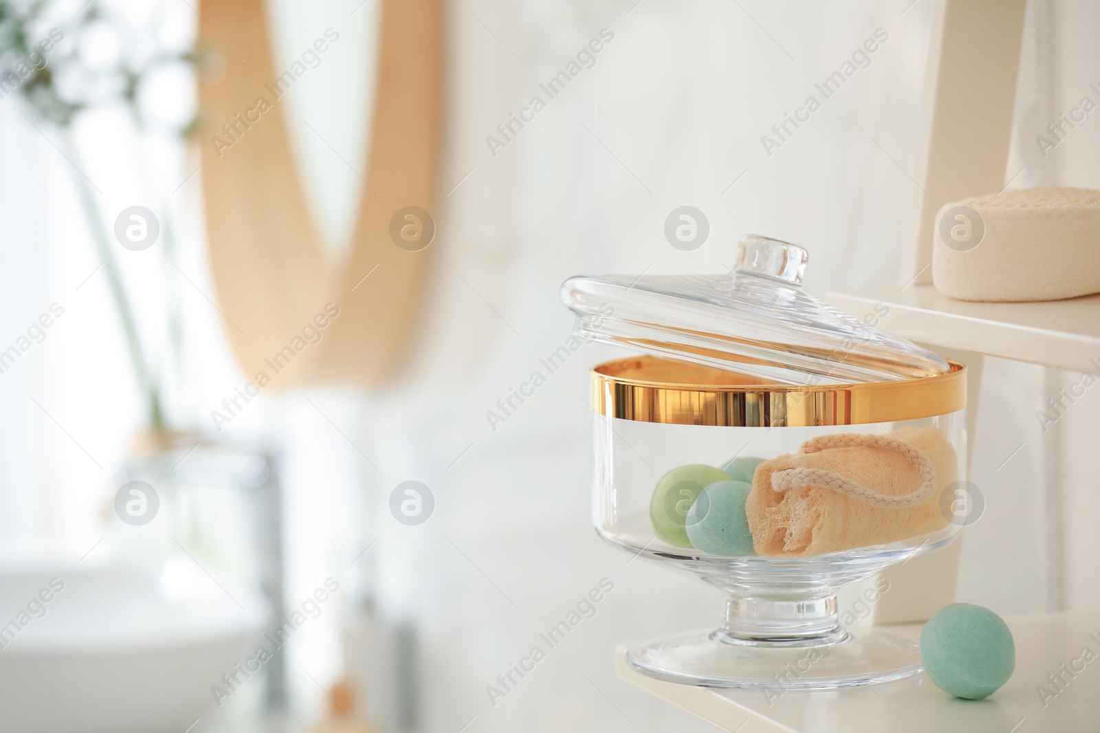 Photo of Jar with bath bombs and loofah sponge on shelving unit in bathroom