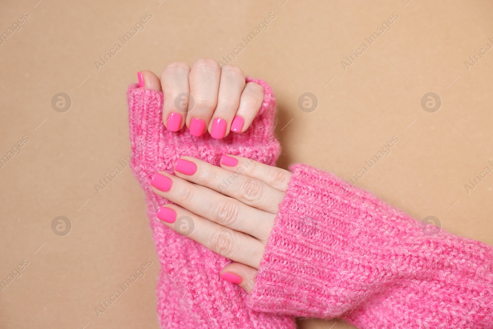 Photo of Woman showing her manicured hands with pink nail polish on dark beige background, top view