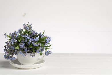 Photo of Beautiful forget-me-not flowers in cup and saucer on wooden table against white background. Space for text