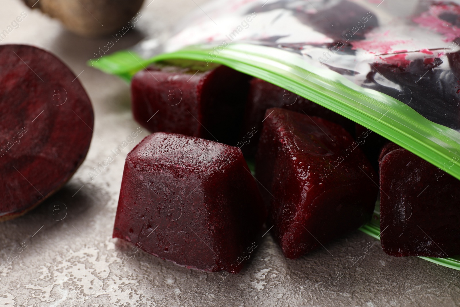 Photo of Frozen beet puree cubes in plastic bag on marble table, closeup