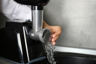 Woman washing electric meat grinder indoors, closeup. Space for text