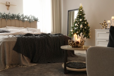 Beautiful decorated Christmas tree with fairy lights in bedroom interior