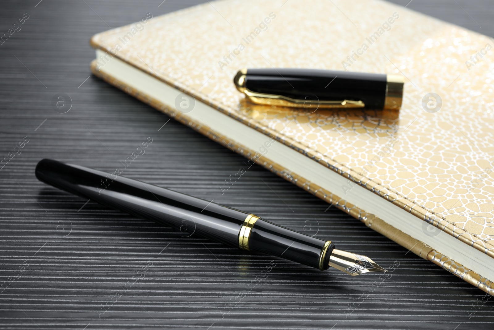 Photo of Stylish fountain pen and notebook on black wooden table, closeup