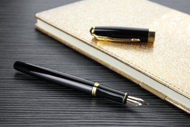 Stylish fountain pen and notebook on black wooden table, closeup
