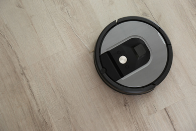 Modern robotic vacuum cleaner on wooden floor, top view. Space for text